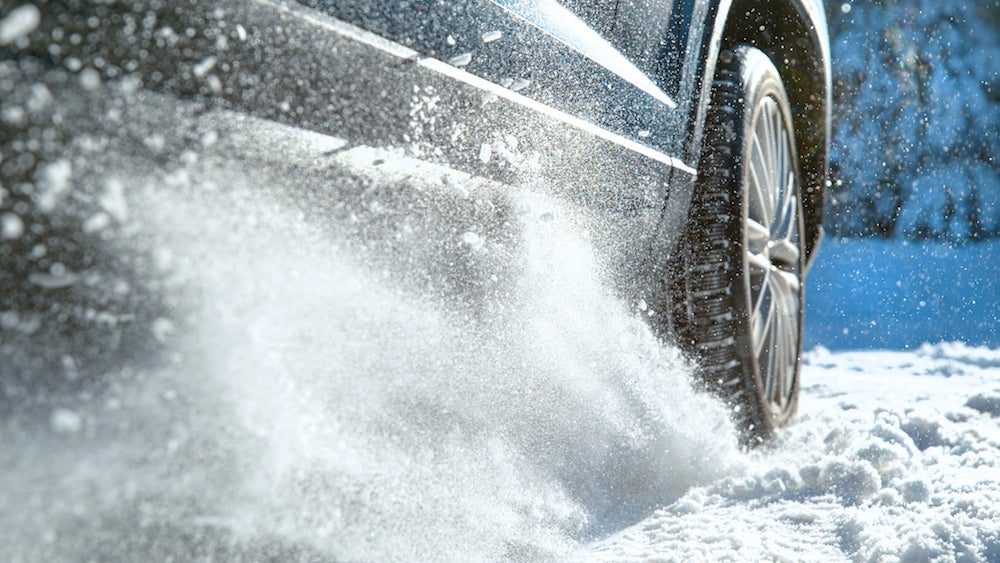 A closeup of a vehicle’s tire kicking up a spray of snow