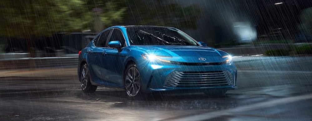 A bright blue 2026 Toyota Camry sedan with its headlights on in the rain