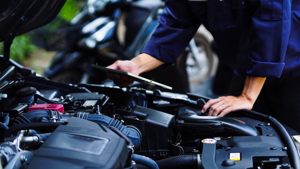 A person in blue coveralls examining the engine of a vehicle