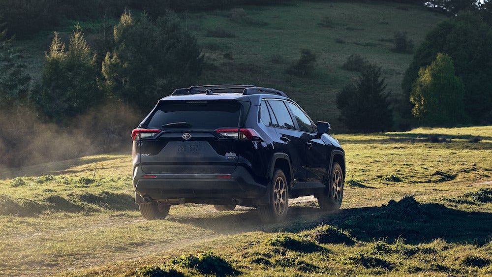 A black 2025 Toyota RAV4 Hybrid SUV driving over a hilly field.