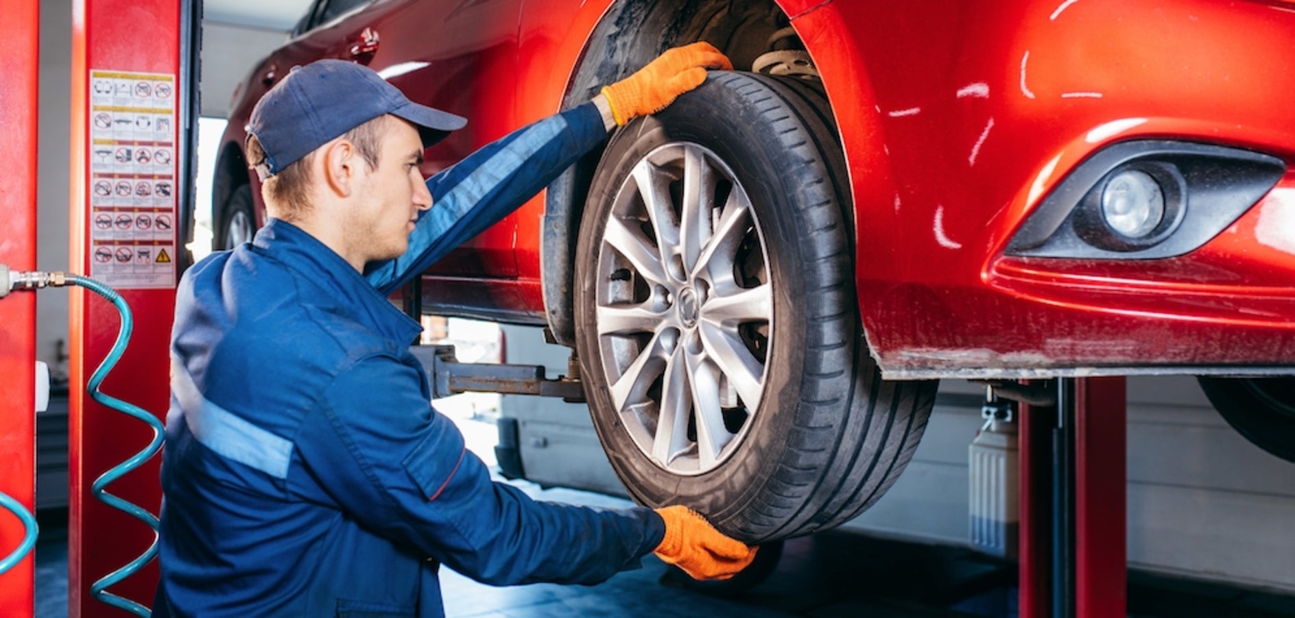 A white person in a blue cap and jumpsuit working on the tires of a red car