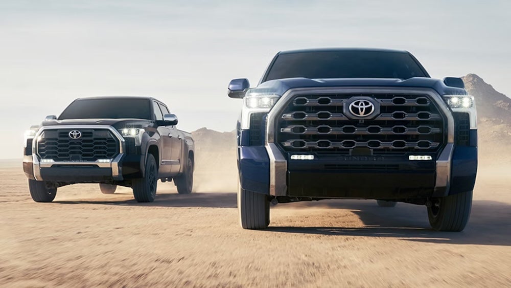 Two 2026 Toyota Tundra pickup trucks, one black and one blue, driving in the desert