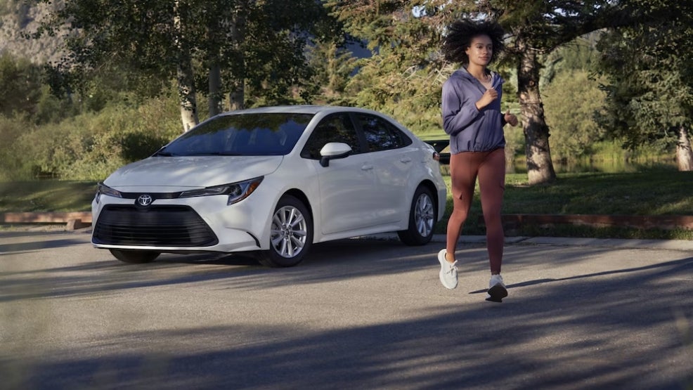 A jogger running near a white 2026 Toyota Corolla sedan