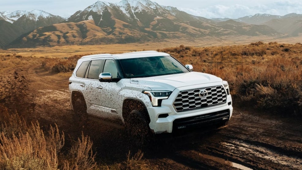 A white 2026 Toyota Sequoia SUV driving down a muddy dirt road